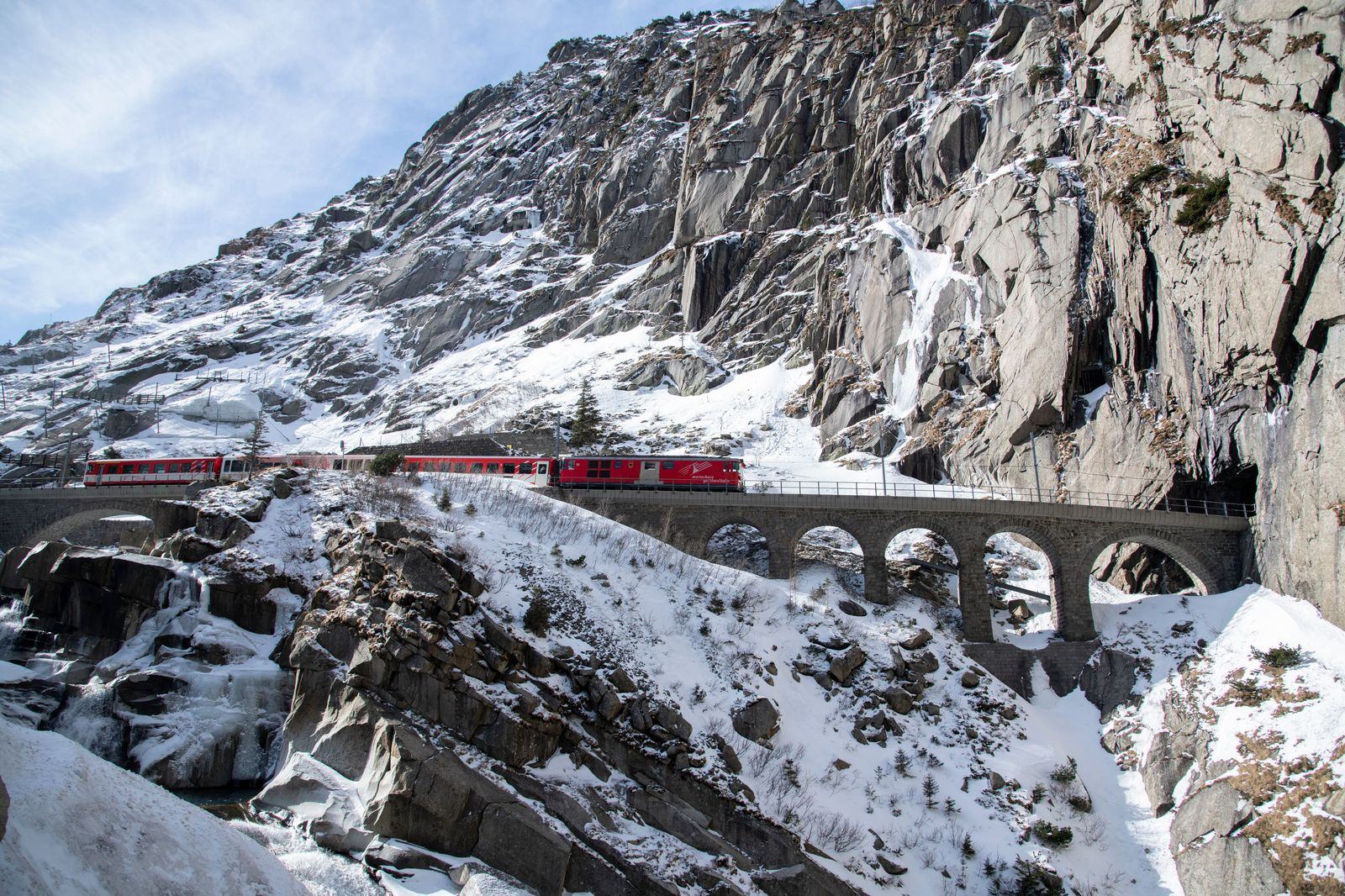 Red mountain train crossing a snowy viaduct in the Alps