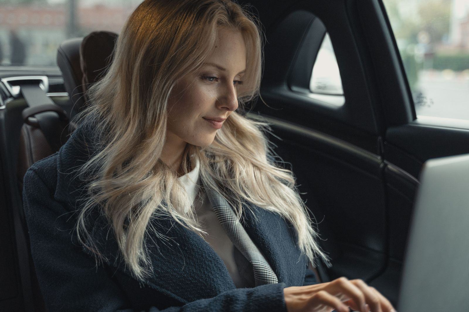Executive working on a laptop in the rear seat of a corporate car between meetings