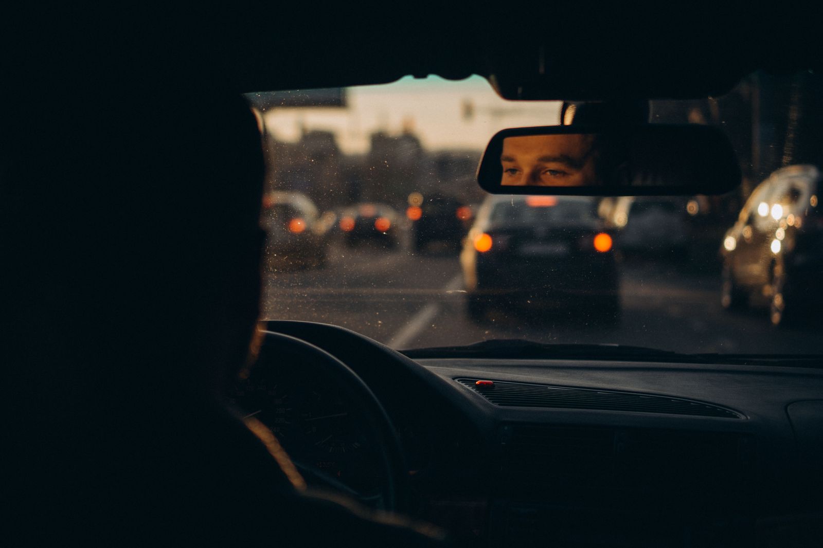 A private chauffeur waiting beside a sedan on a city street in the evening